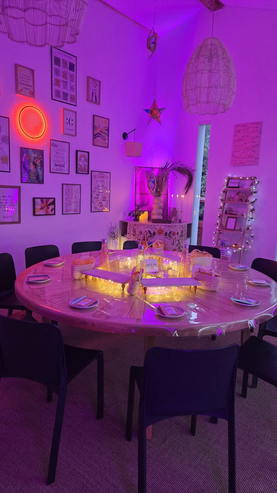 Salle du cercle avec son mur de cadres, son néon en forme de soleil et sa table ronde éclairée aux bougies